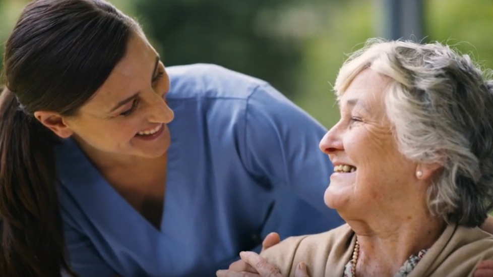 Female health care worker exchanging smiles with elderly woman
