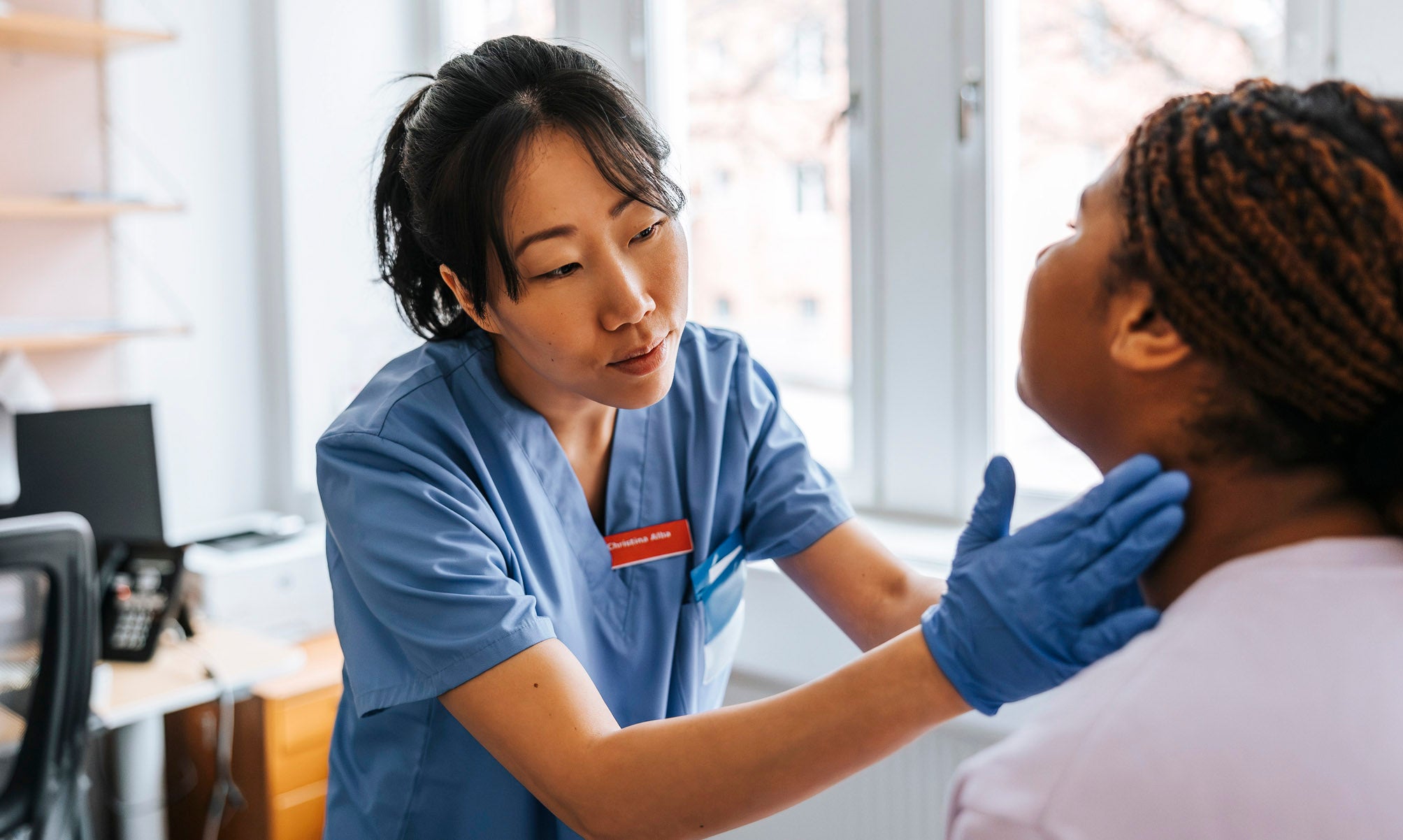 Female medical expert checking lymph nodes of young patient in examination room at hospital