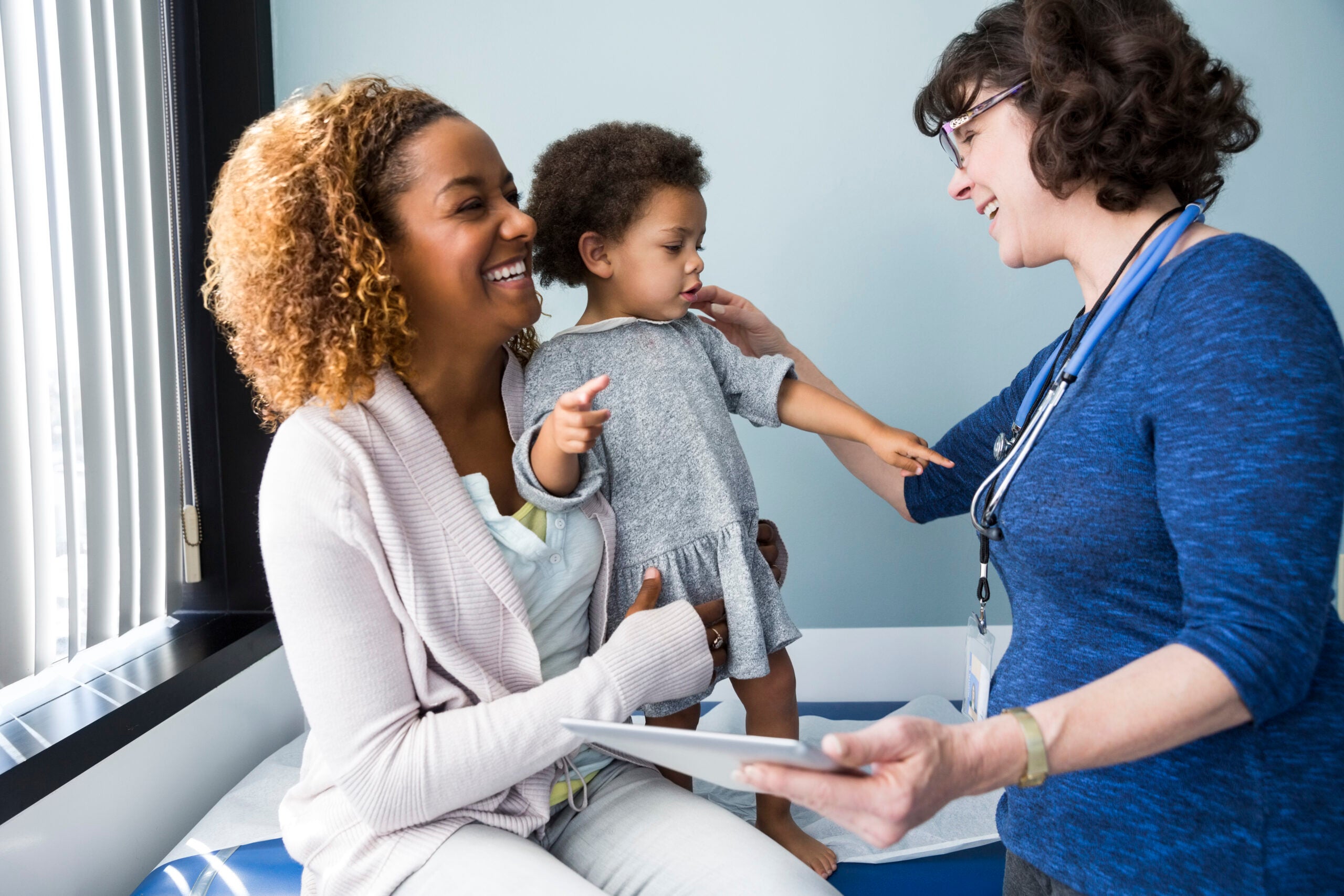 Smiling pediatrician showing digital tablet to mother and baby in exam room